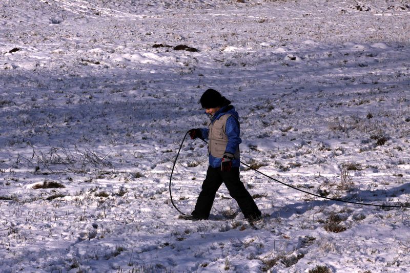 Chlapec táhnoucí v ruce za sebou lanko ve sněhu