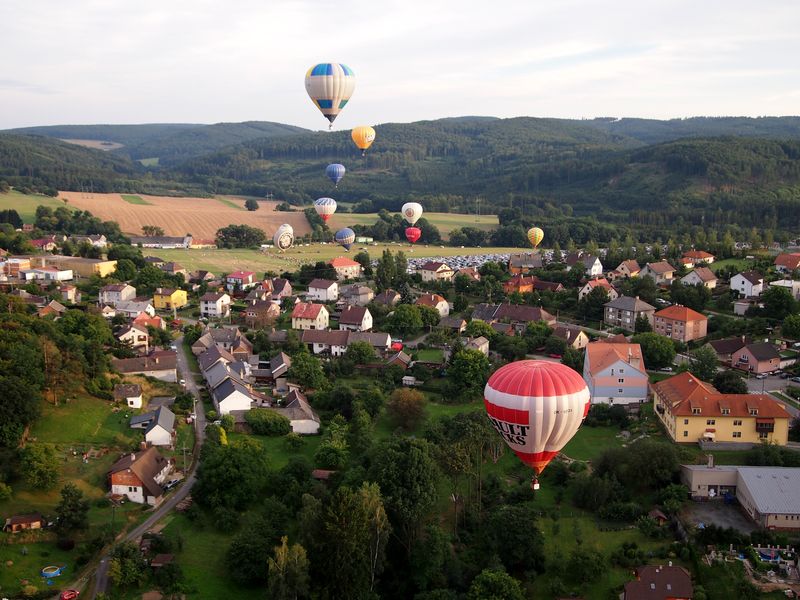 Balóny, které spolu letí nad vesničkou s výhledem na přírodu